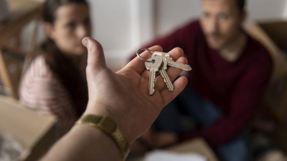 Hånd holder nøkkelknippe foran et sittende par.